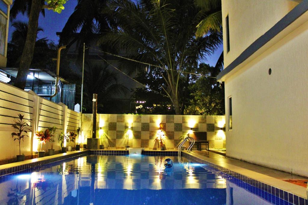 a swimming pool at night with a building and palm trees at Wotel Calangute Goa in Calangute