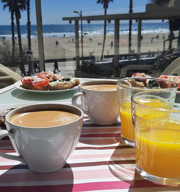 a table with two cups of coffee and drinks on a beach at FiveStepsToSea - Beach Apartment Valencia in Valencia