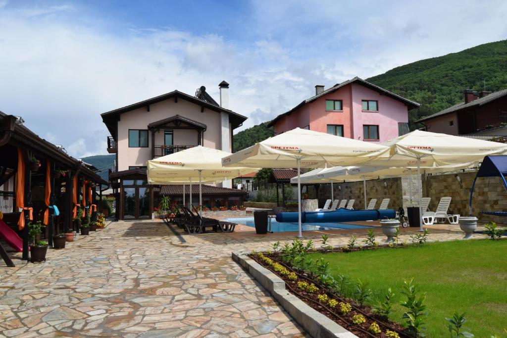 a patio with umbrellas and a pool and buildings at Asya Guest House in Sapareva Banya