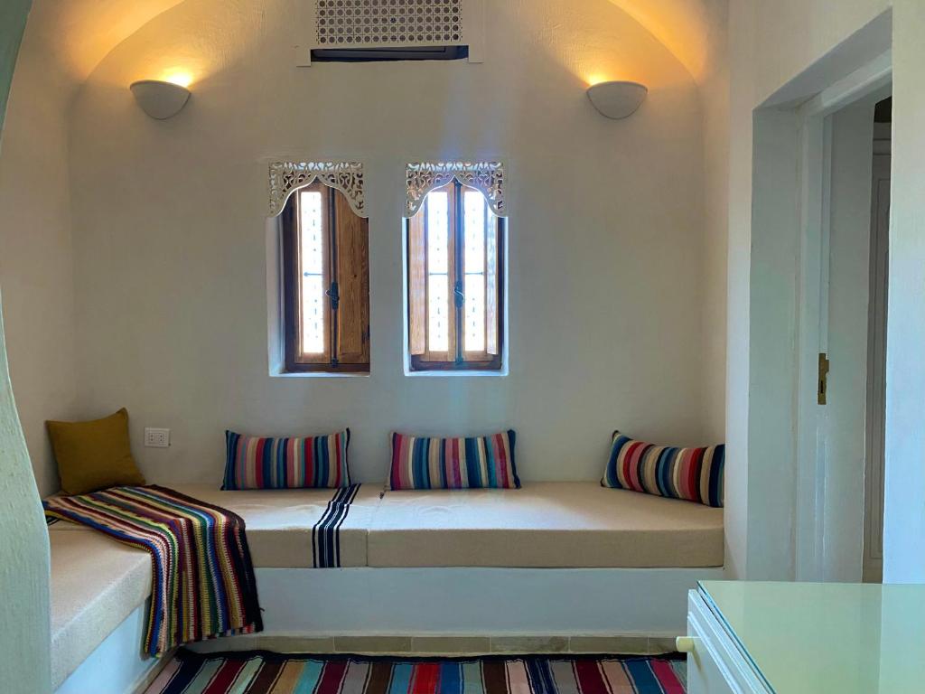 a room with a bench with pillows and two windows at Hôtel Djerba Authentique - Au centre de Midoun in Midoun