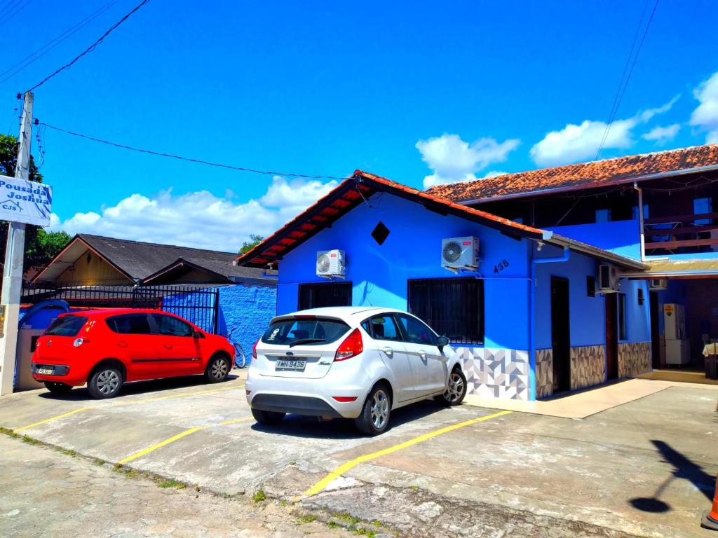 deux voitures garées dans un parking devant un bâtiment bleu dans l'établissement Pousada JOSHUA, à Penha