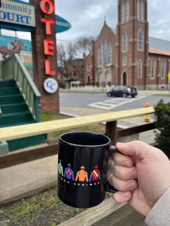 una persona sosteniendo una taza de café frente a un edificio en Community Court Motel, en Saratoga Springs