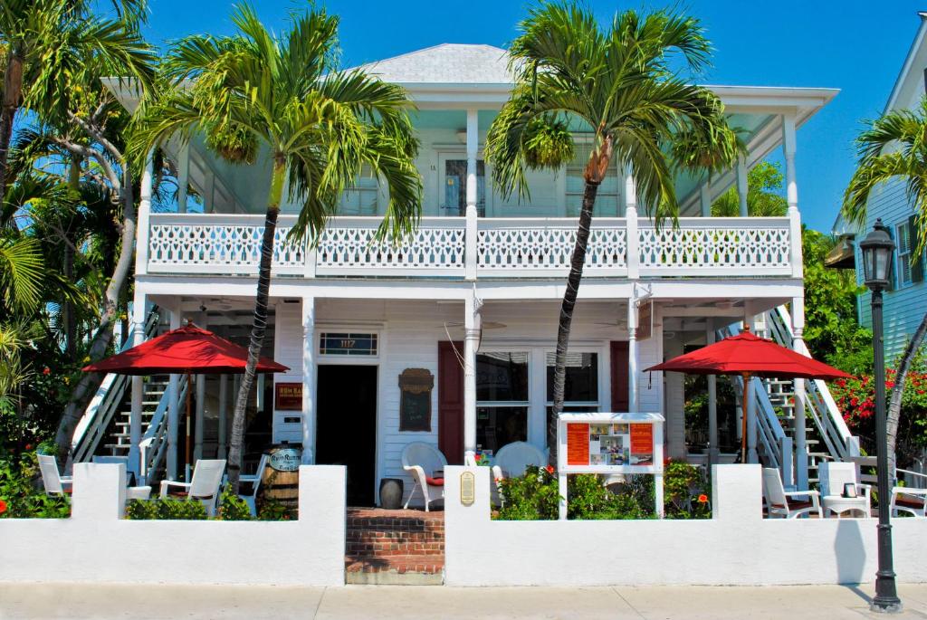 uma casa branca com palmeiras e guarda-sóis vermelhos em The Speakeasy Inn and Rum Bar em Key West