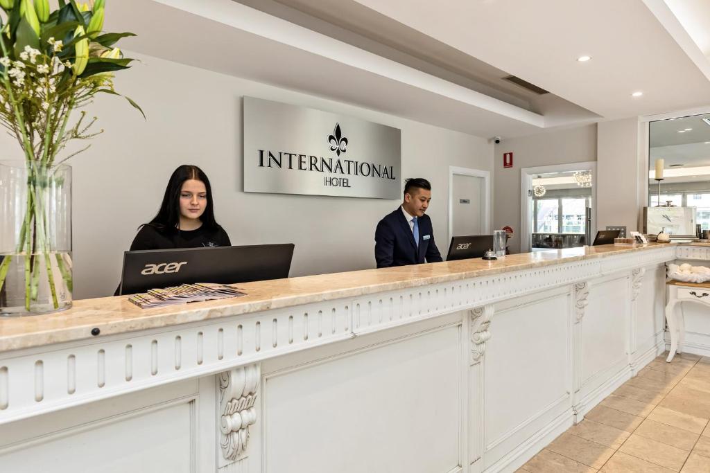 dwie osoby stojące przy recepcji przy biurku informacyjnym w obiekcie International Hotel Wagga Wagga w mieście Wagga Wagga