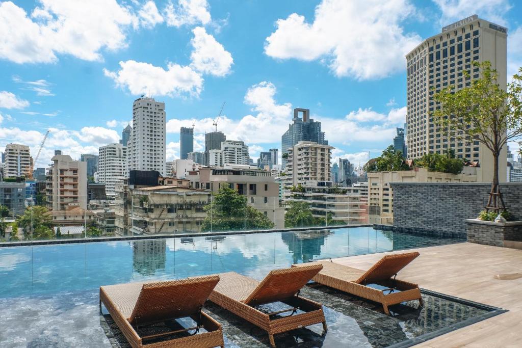 a swimming pool with two chairs and a city skyline at The Coach Hotel Sukhumvit - Asok BTS Bangkok in Bangkok