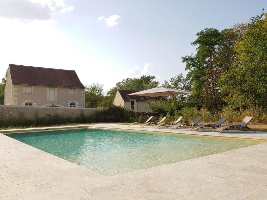 une piscine avec des chaises longues et une maison dans l'établissement Le Domaine des Cyclamens, à Verneuil-sur-Indre