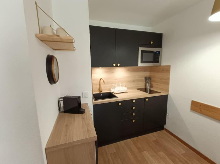 una pequeña cocina con armarios negros y microondas en Snowliday - Appartement Rénové en résidence 4* pour 4 pers. Valmeinier 1900 en Valmeinier
