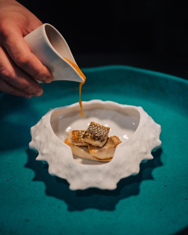 a person pouring syrup onto a plate of food at Porto Covo Praia Hotel & SPA in Porto Covo