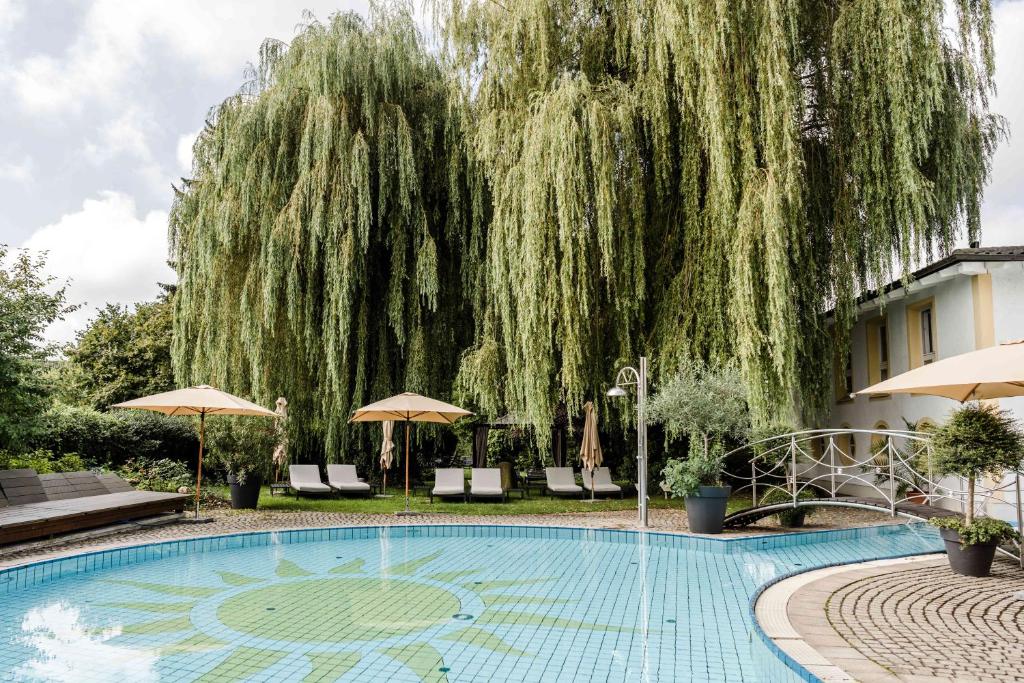 a weeping willow tree towering over a swimming pool at Hotel Antoniushof in Ruhstorf