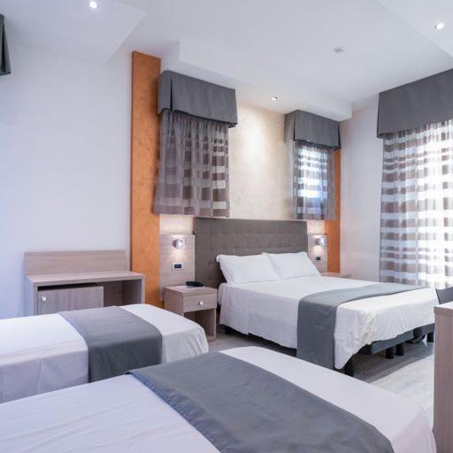a hotel room with two beds and two windows at Hotel Gabbiano in Rimini