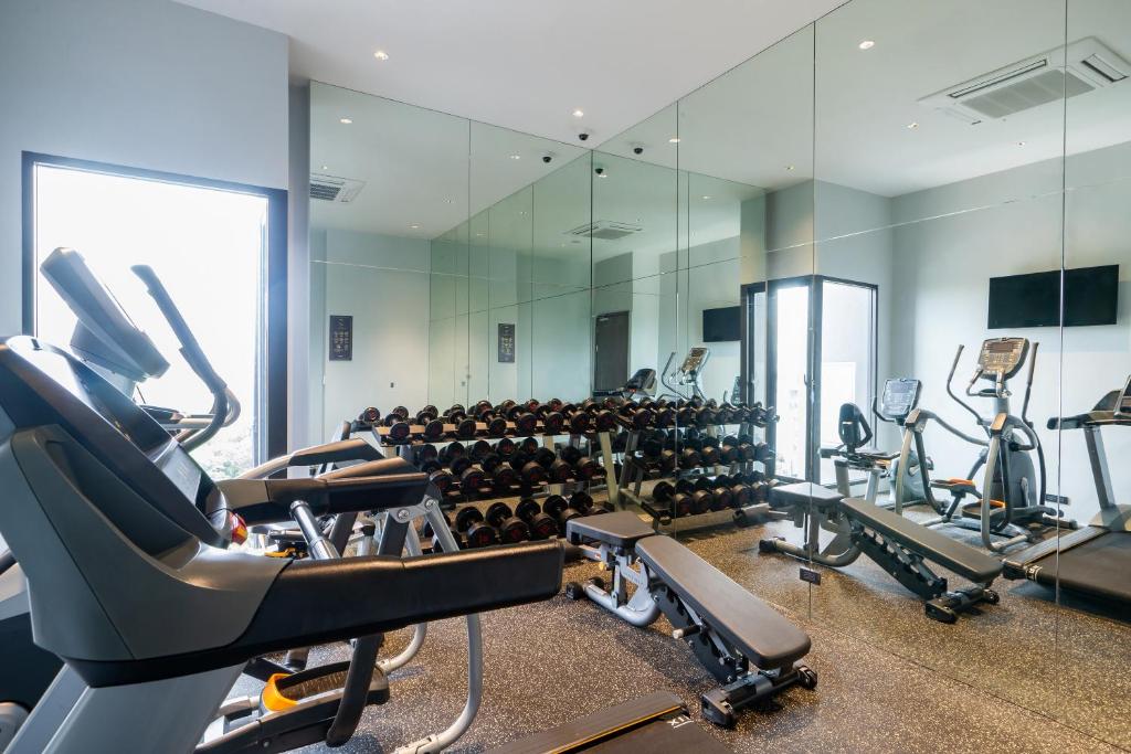 A compact mirrored gym with cardio machines, free weights, and a bench.