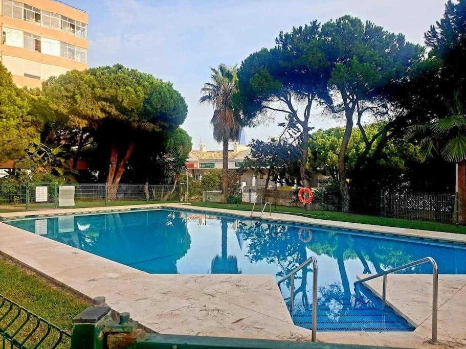 a large blue swimming pool with trees and a building at Precioso estudio con piscina a 200m del mar in Marbella
