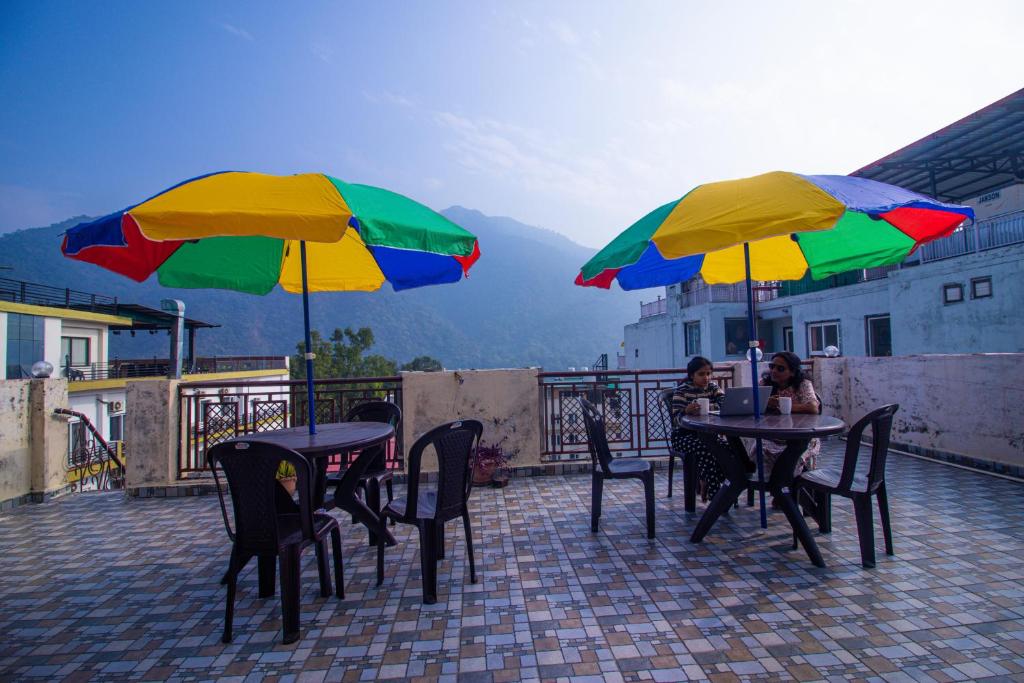 two people sitting at tables with umbrellas on a balcony at Triple One Hostel Tapovan Rishikesh in Rishīkesh