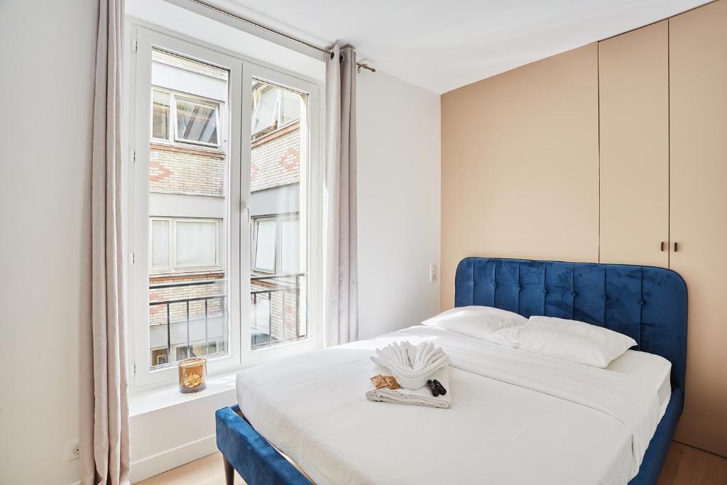 a bed with a blue headboard and a window at Apartment Louvre Museum by Studio prestige in Paris