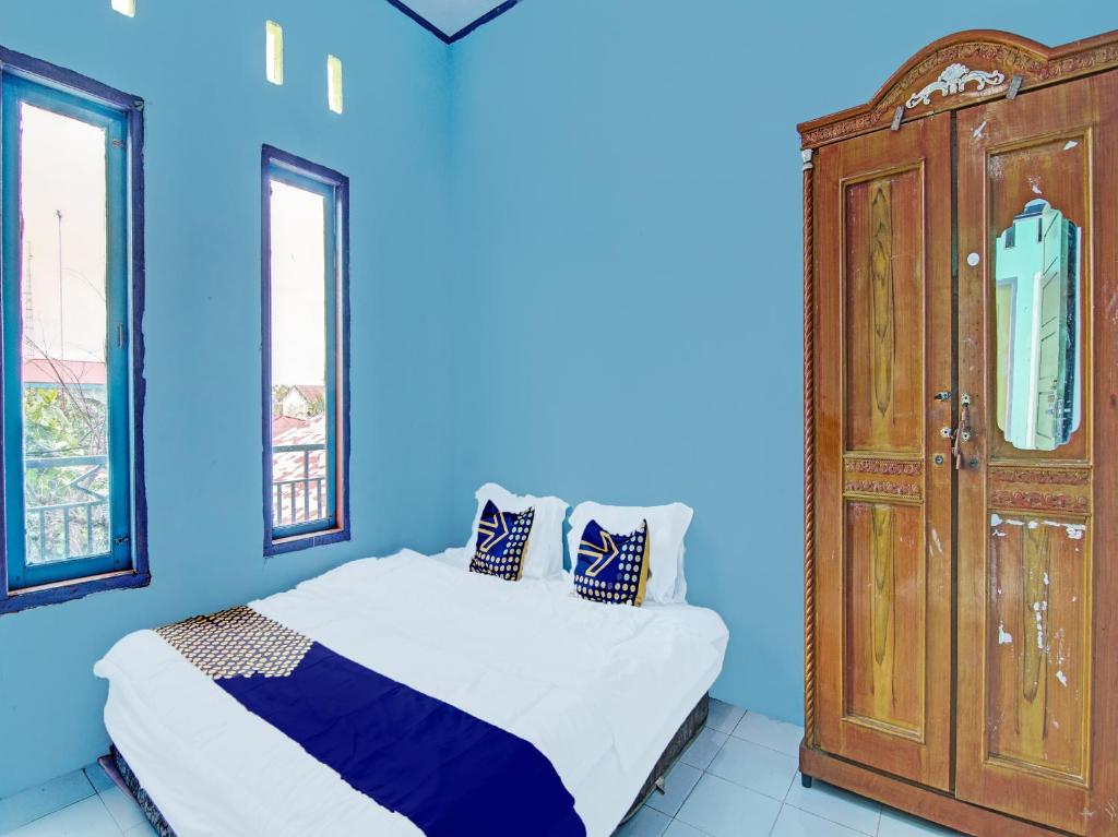 SPOT ON 91918 Najla Guest House Syariah في Parit: غرفة نوم زرقاء مع سرير وخزانة خشبية