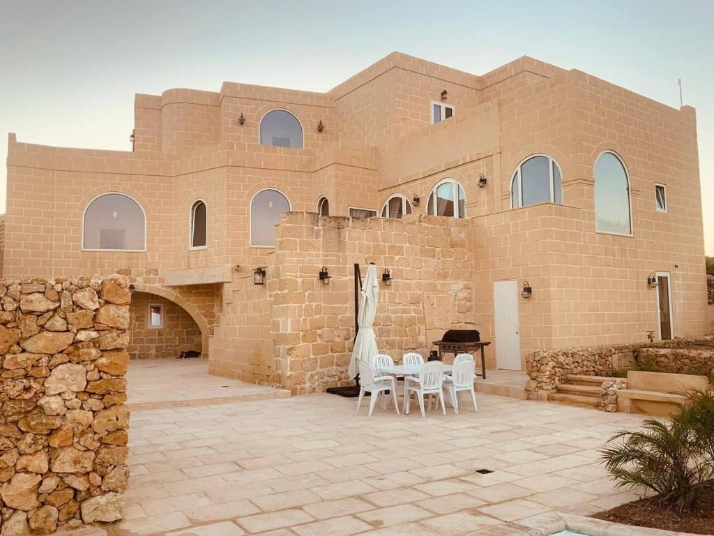 ein Backsteingebäude mit Tischen und Stühlen davor in der Unterkunft Farmhouse Villa in Gozo with large pool & garden in Birbuba