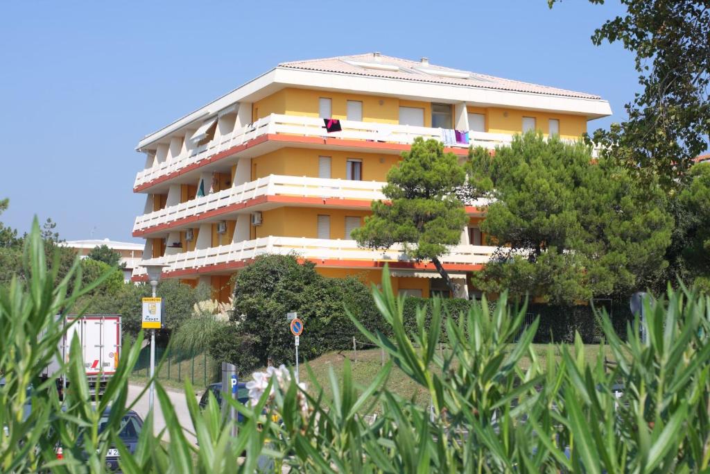 un bâtiment jaune avec des arbres devant lui dans l'établissement Condominio Carina Sud, à Bibione