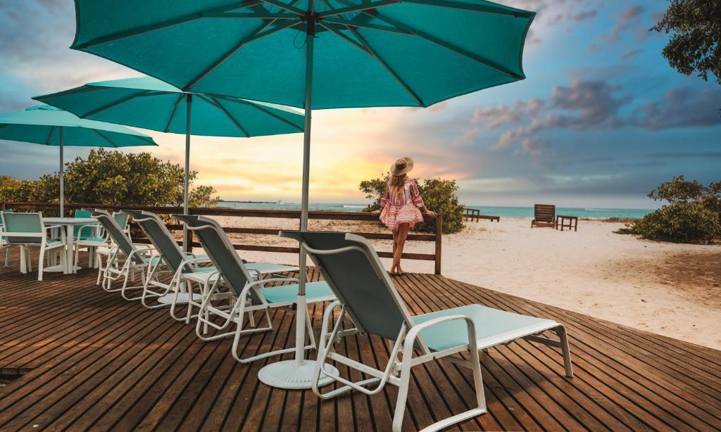 una mujer parada en una playa con sillas y sombrillas en Isamar Hotel en Puerto Villamil