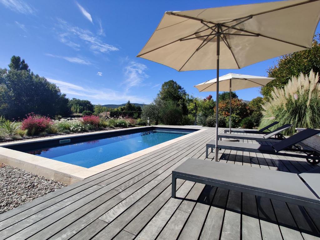 a patio with an umbrella and chairs and a pool at Le Mas des 3 Tilleuls in Malaucène