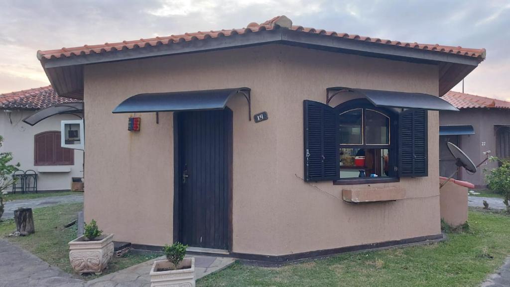 une petite maison avec des volets noirs dans l'établissement Chalé Pé na Areia em Rio das Ostras, à Rio das Ostras