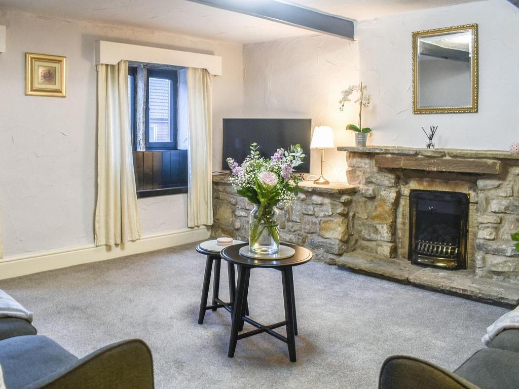 a living room with a fireplace and a vase of flowers at Chattox Cottage in Barrowford