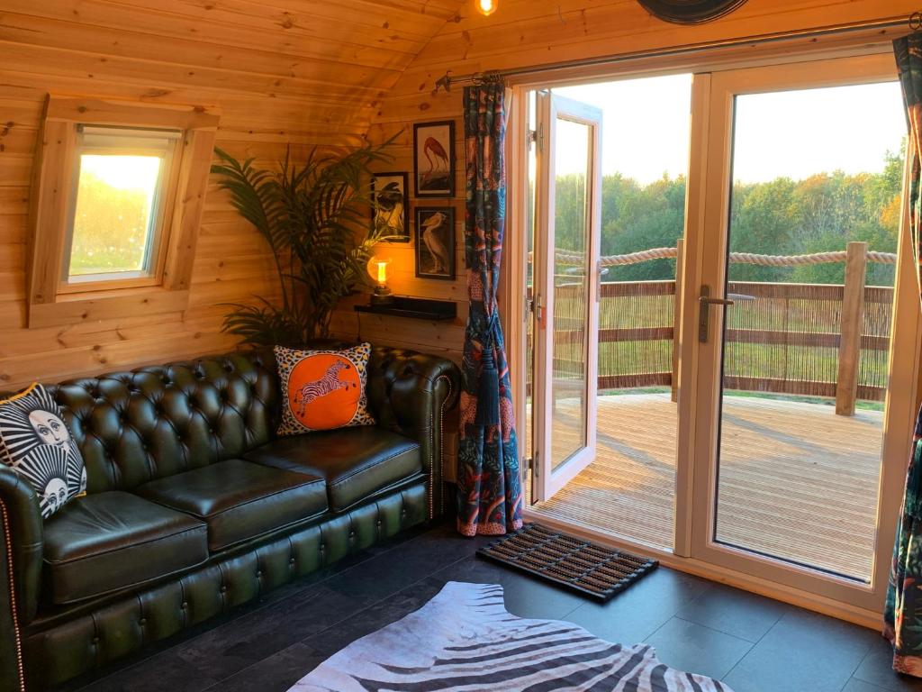 a living room with a leather couch and a deck at Fox’s Furrow Quirky Glamping Pod with Private Hot Tub 