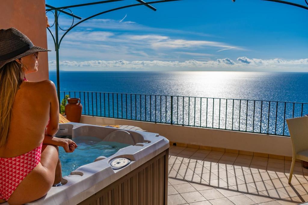 una mujer sentada en una bañera de hidromasaje en un balcón con vistas al océano en Casalbivio Positano, en Positano