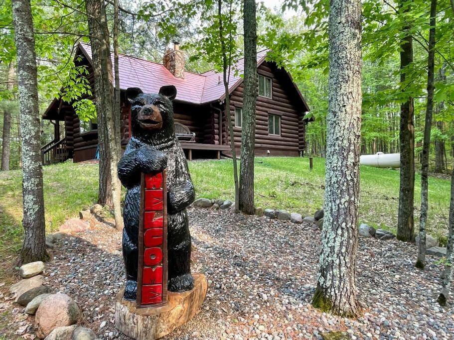 una estatua de un oso de pie en un tronco frente a una cabaña en Camp Voyager Log Cabin resort pool, golf, trails, lakes more, en Webb Lake