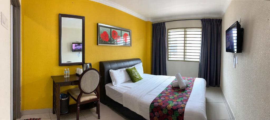 a bedroom with a bed and a desk and yellow walls at Lumuda Hotel in Lumut