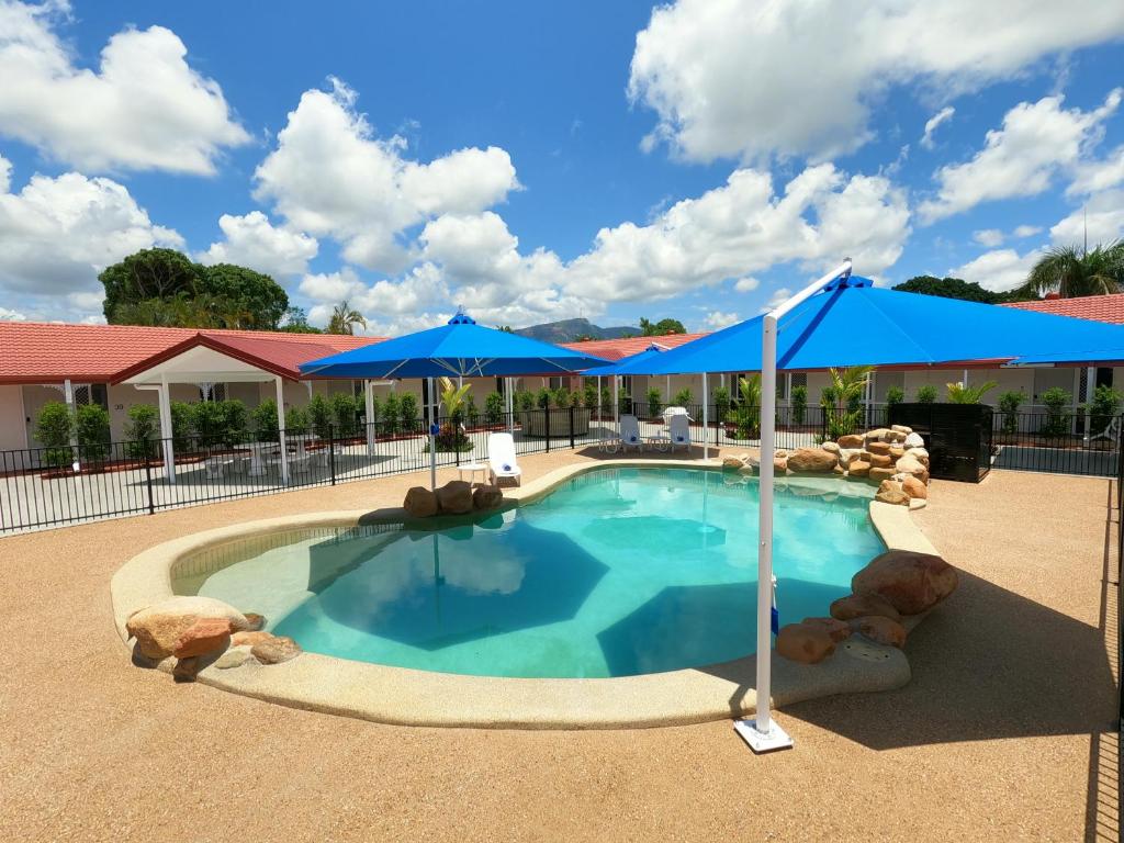 ein Pool mit blauen Sonnenschirmen in einem Resort in der Unterkunft Monte Carlo Motor Inn in Townsville