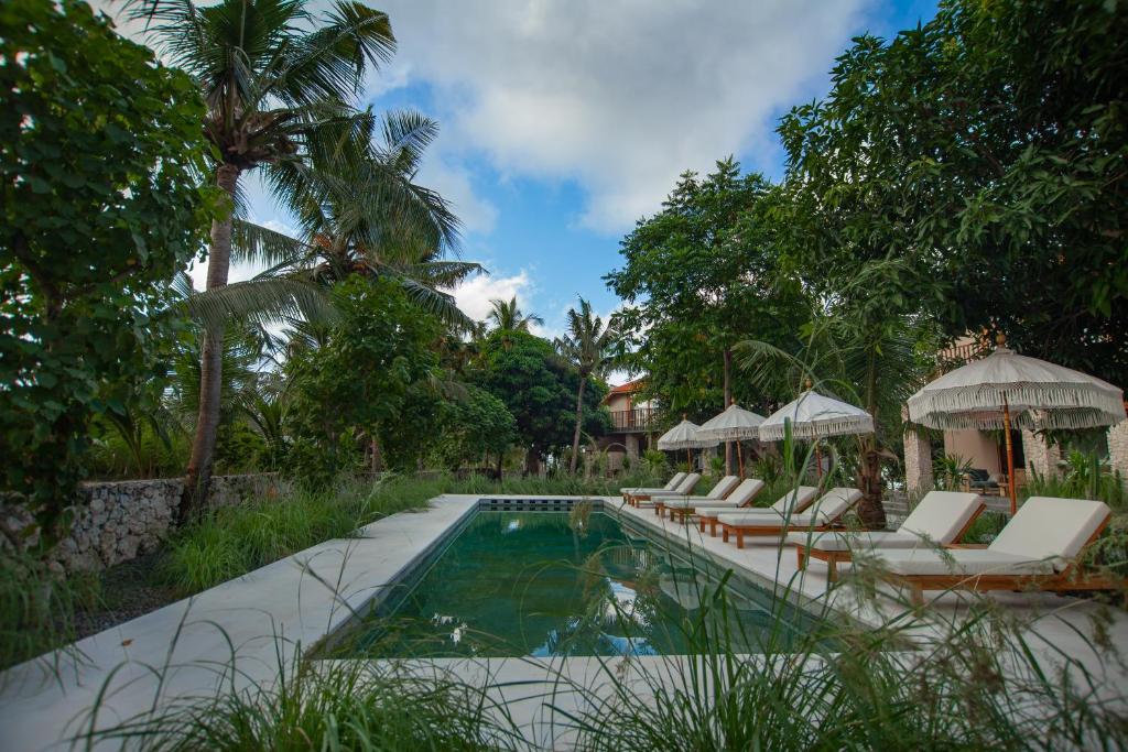 a swimming pool with lounge chairs and umbrellas at Diamond Beach Villas in Nusa Penida
