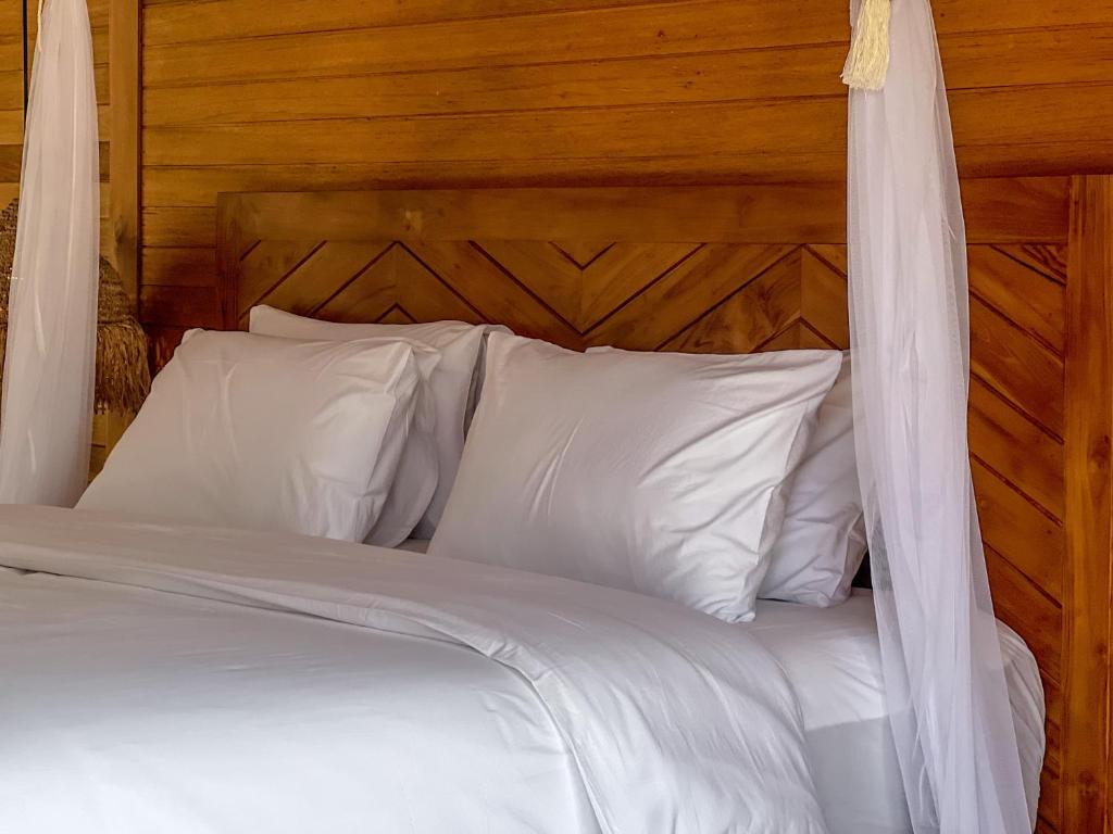 a bed with white pillows and a wooden headboard at Diamond Beach Villas in Nusa Penida