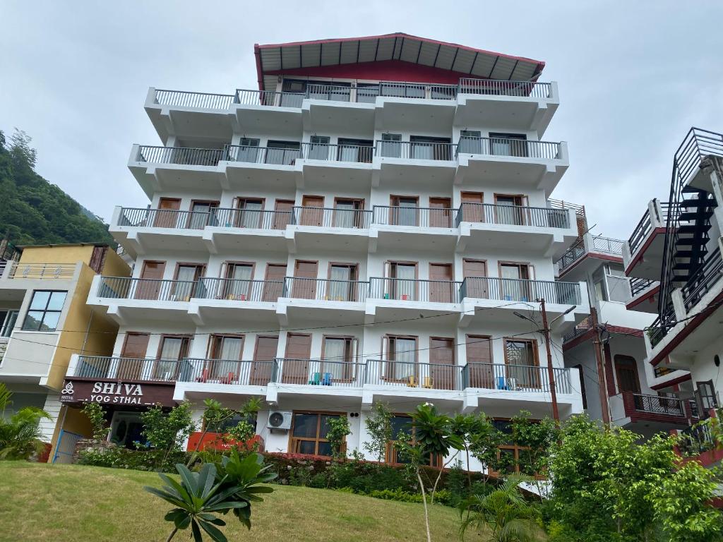 a tall white building with balconies and trees at Hotel Shiva Yog Sthal in Rishīkesh