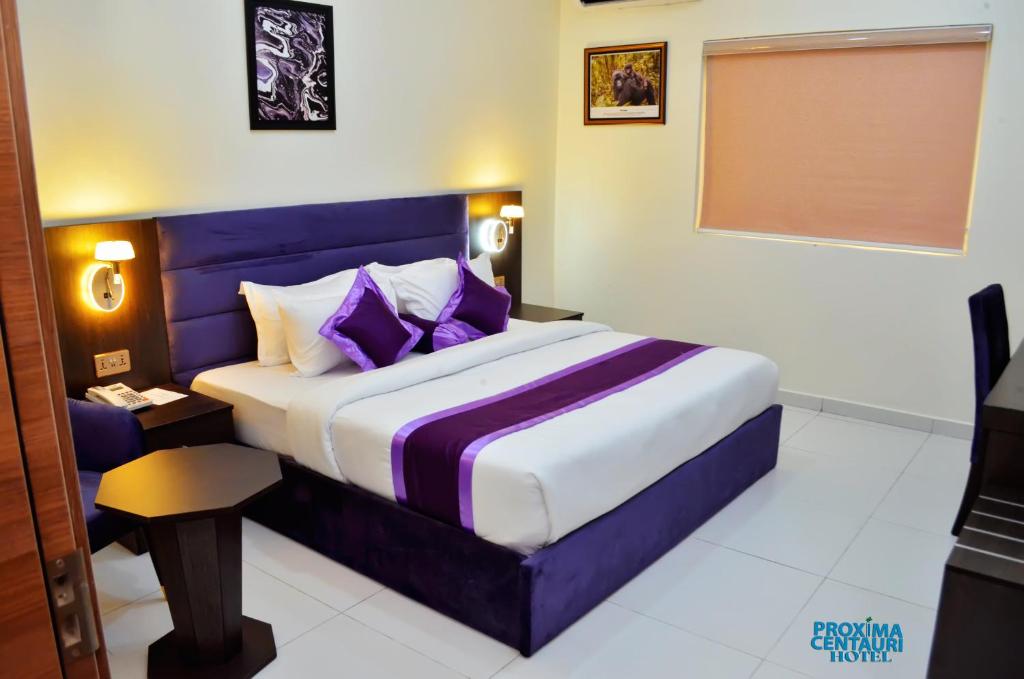 um quarto com uma cama king-size e almofadas roxas em Proxima Centauri Hotel em Port Harcourt