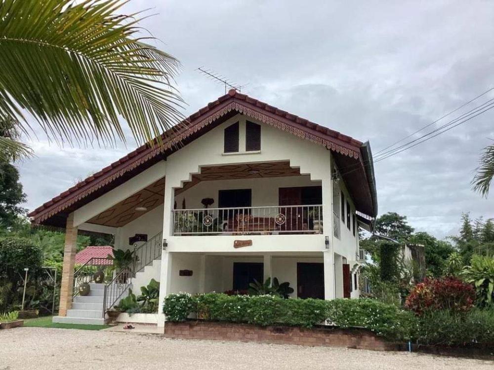 a white house with a balcony and a palm tree at Nantawanhomestay in Lampang