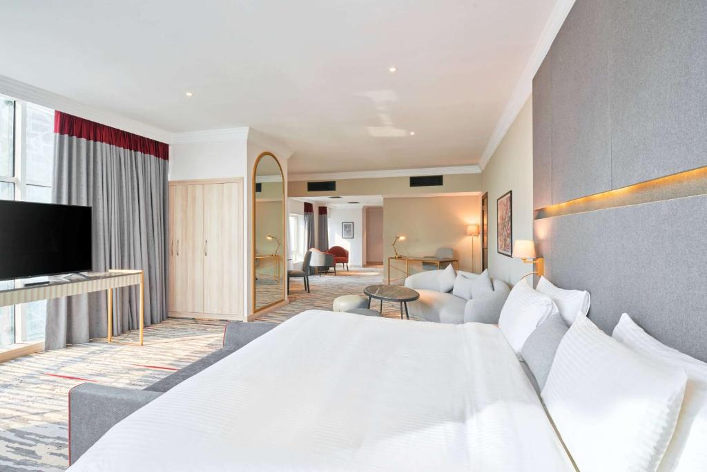 Ramada by Wyndham Doha Old Town في الدوحة: غرفة نوم بسرير ابيض كبير وغرفة معيشة