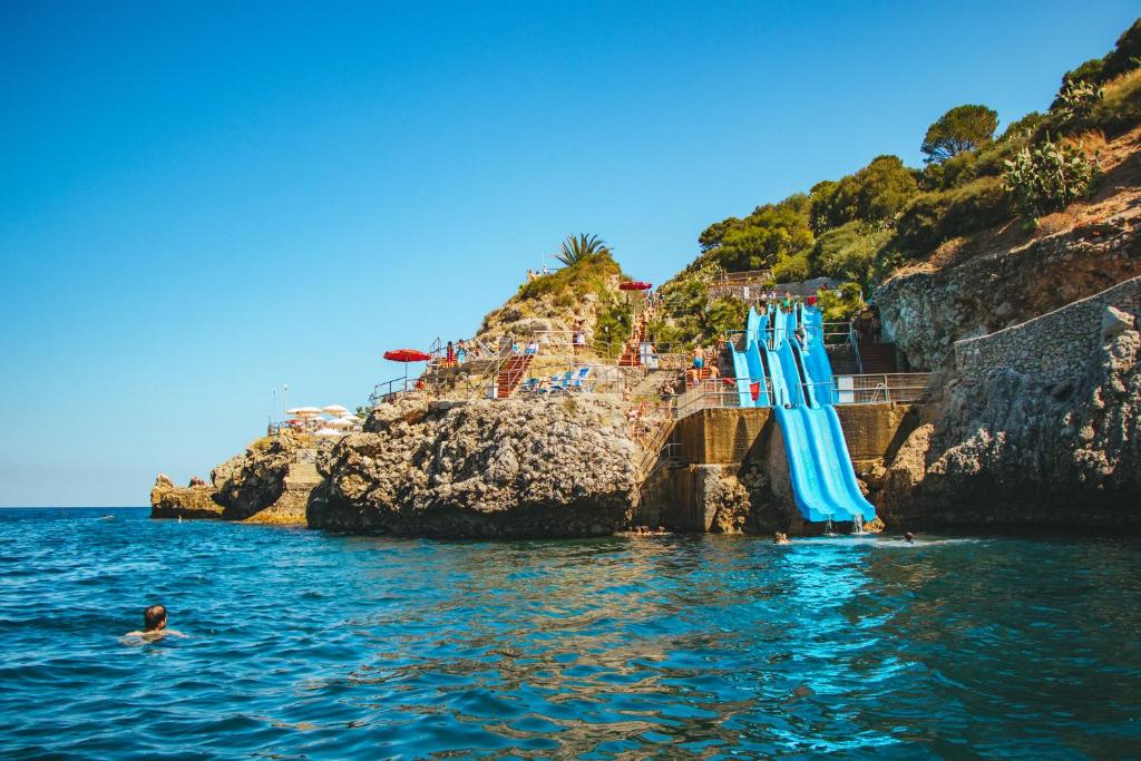 a group of blue umbrellas in the water next to a cliff at CDSHotels Terrasini - Città del Mare in Terrasini