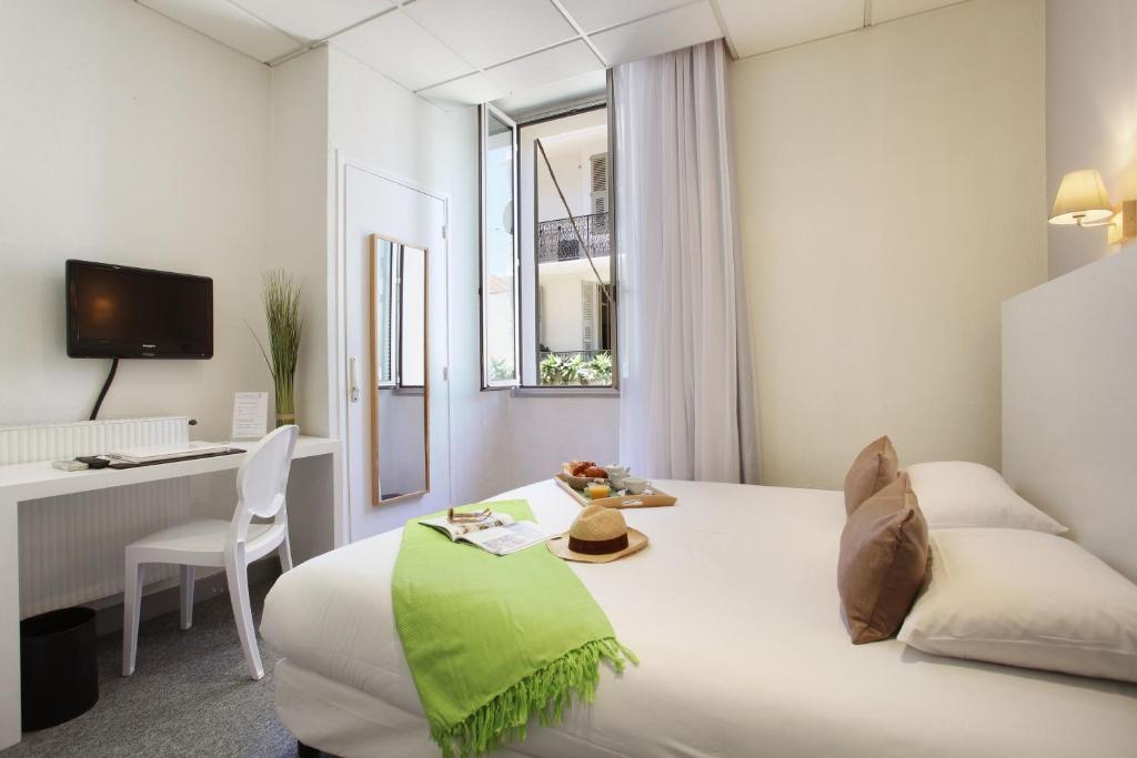 a white hotel room with a bed and a desk at Hôtel P.L.M. in Cannes