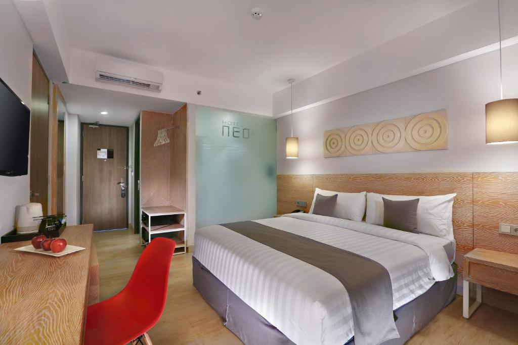 レギャンにあるHotel NEO+ Kuta Legian by ASTONの大きなベッドと赤い椅子が備わるホテルルームです。