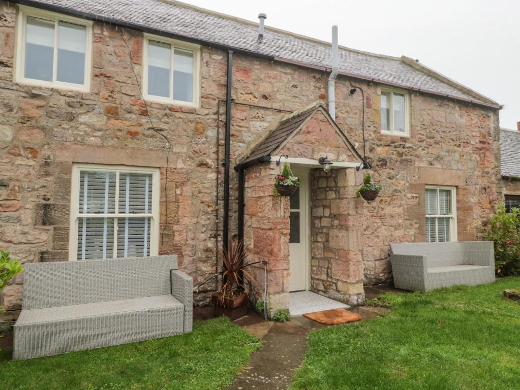 a brick house with two benches in front of it at Donni Hall Cottage in Chathill