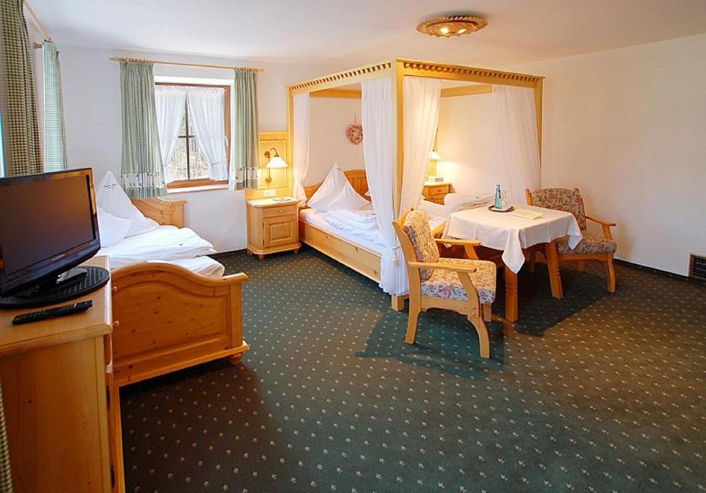 a room with two beds and a table and a television at Landhaus Degen in Bischofswiesen