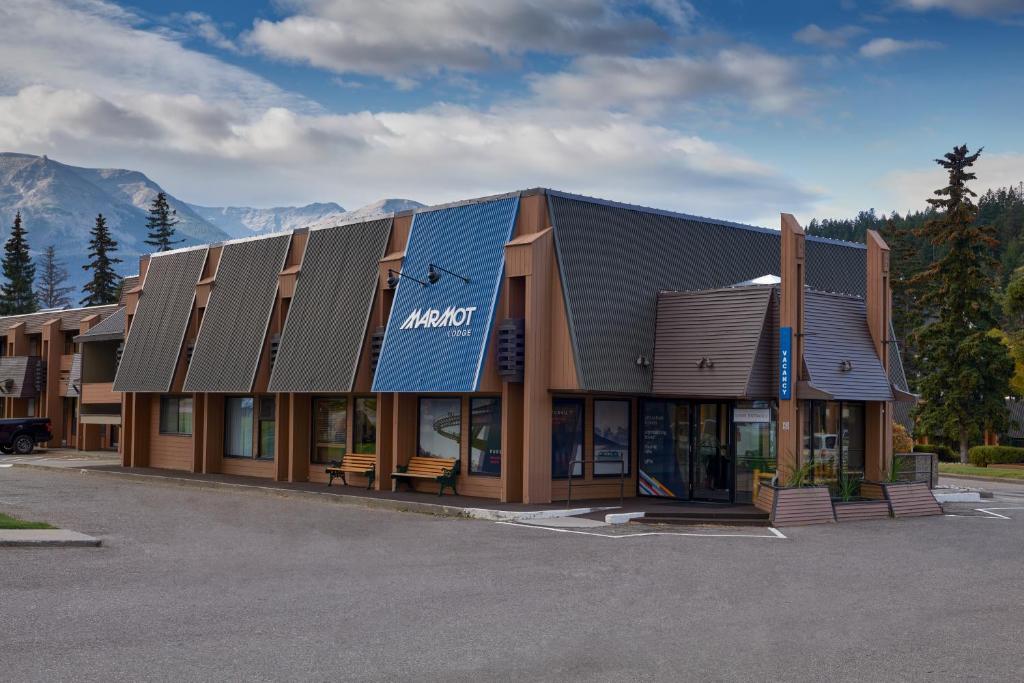 a large building in a parking lot with mountains at Marmot Lodge Jasper in Jasper