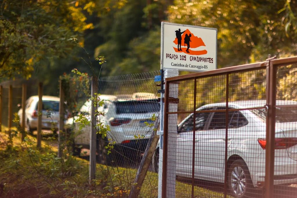 ein Schild an einem Zaun mit Autos auf einem Parkplatz in der Unterkunft Caminhos de Caravaggio - Hostel Parada dos Caminhantes in Nova Palmira