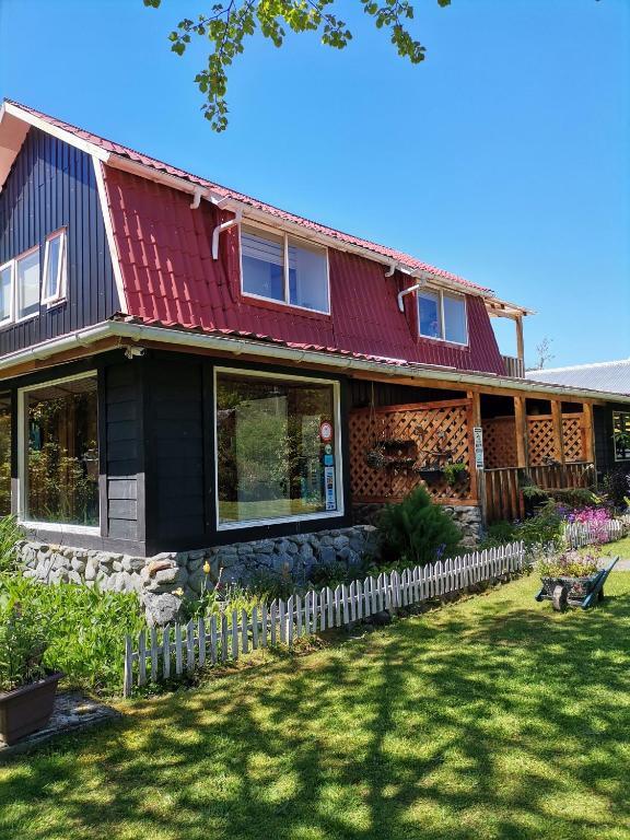 une maison avec un toit rouge et une clôture blanche dans l'établissement Departamento Rossbach, à Puerto Puyuhuapi