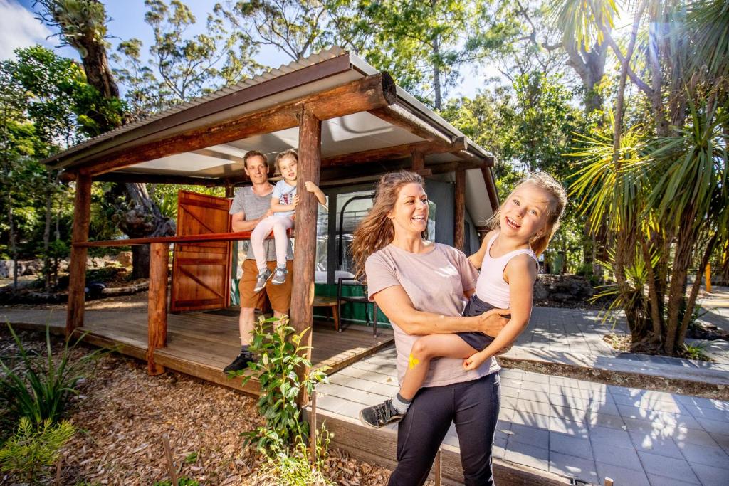 una famiglia che si trova di fronte a una piccola casa di Binna Burra Rainforest Campsite a Beechmont