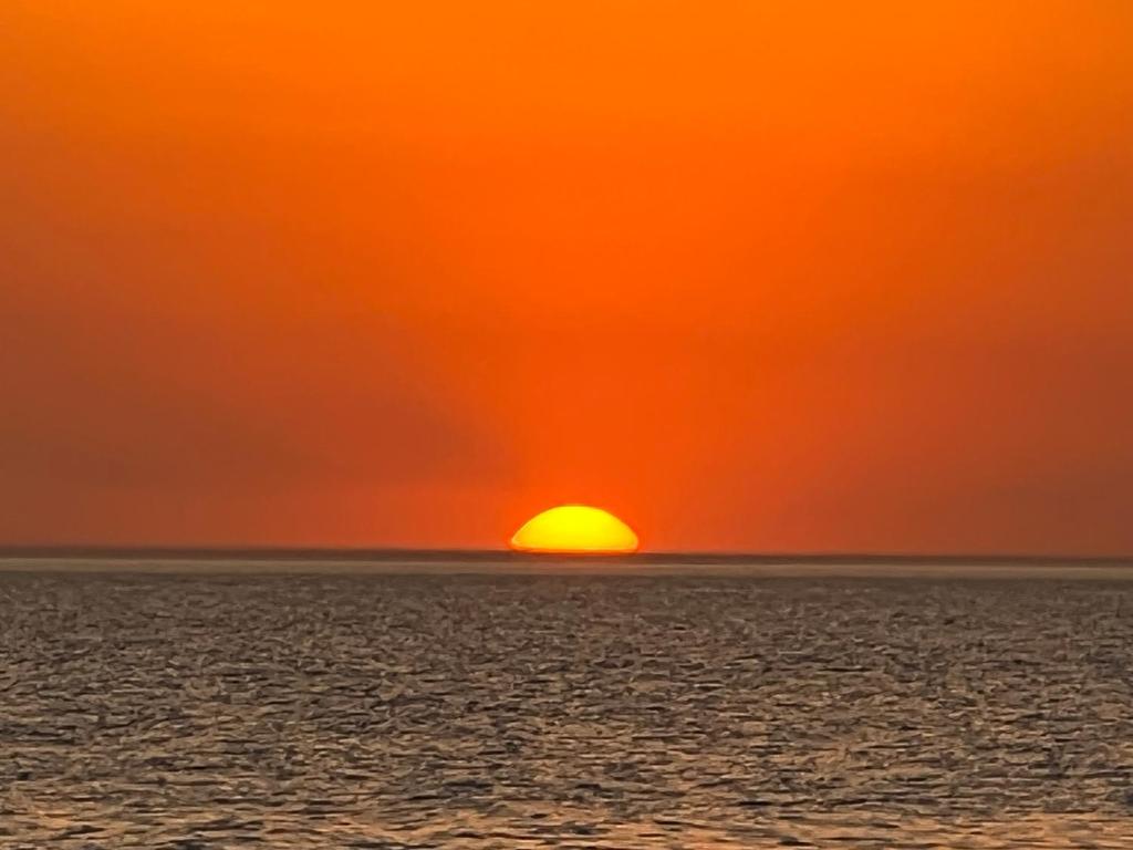 una puesta de sol naranja sobre el océano con el sol en el cielo en Sol y mar, en Monte Hermoso