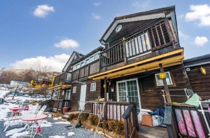 a wooden house with a deck in the snow at Gilson Story Pension in Pyeongchang