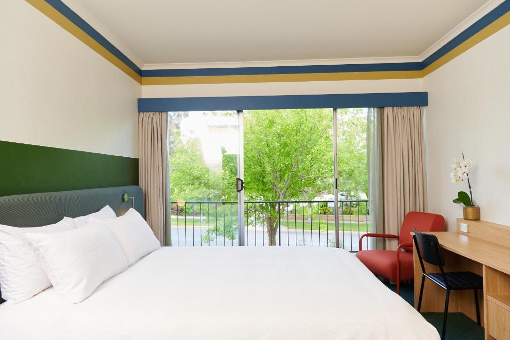 a bedroom with a bed and a desk and a large window at Statesman Hotel in Canberra
