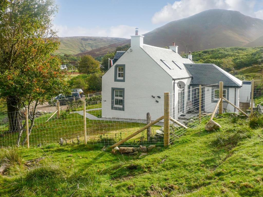 a white house on a hill with mountains in the background at Sqlarran Cottage in Lochranza