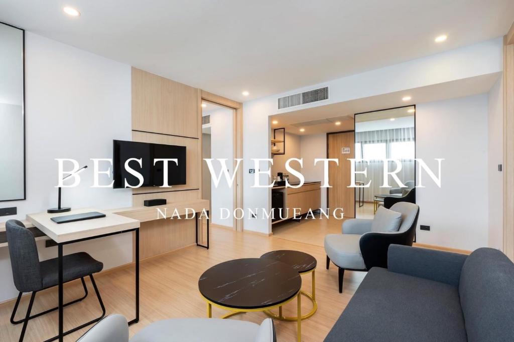 A compact hotel lounge or meeting suite with a desk, television, sofa and armchairs.